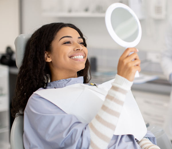 Patient examining smile in mirror after hygiene appointment